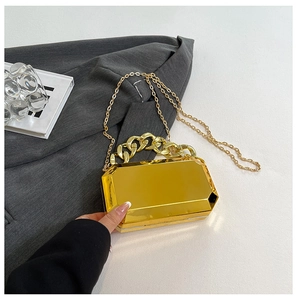 Detailed close-up of golden acrylic geometric clutch bag with thick chain and mirror finish