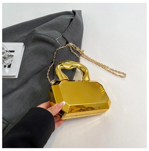 Detail of gold mirror acrylic box bag with geometric cut and twisted handle texture
