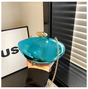 Detail of teal acrylic hard shell clutch bag with gold metallic clasp and chain strap