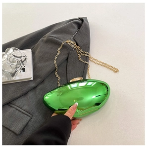 Detail of green metallic oval clutch bag with gold chain strap on a designer background