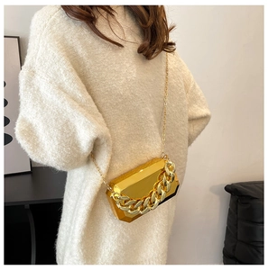 Detail of gold geometric acrylic box bag with chunky chain shown on a white knit sweater