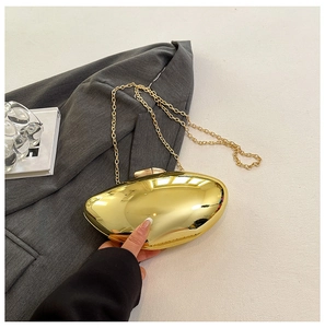 Close-up of a polished gold metallic clutch bag with a sleek chain strap on a textured surface