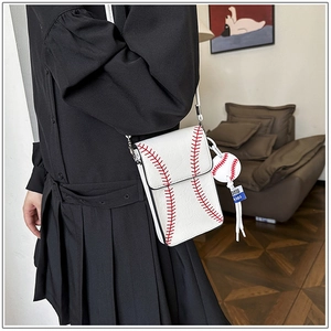 Detailed shot of white baseball-themed crossbody bag with red stitching and charm accessory