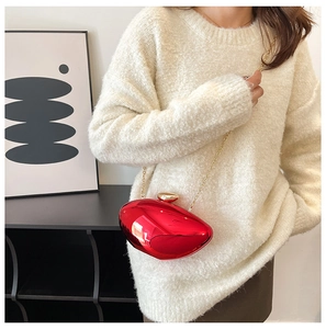 Detail of red acrylic mango evening bag with gold chain strap on a white knit sweater