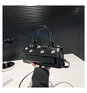 Détail d'un sac à main noir brillant avec rivets argentés et poignées de style urbain