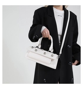Gros plan sur un sac cabas blanc brillant avec de gros clous argentés et cuir lisse