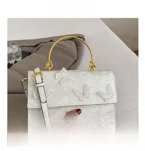 Close-up of white lace shoulder bag with 3D butterfly embroidery and gold metal handle