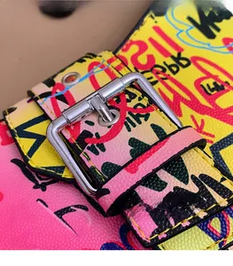 Close-up of pebble leather shoulder bag with colorful graffiti prints and silver metal buckle