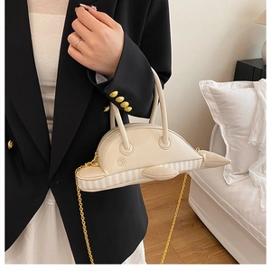 Detail view of cream dolphin shaped handbag with vertical striped base and gold chain strap