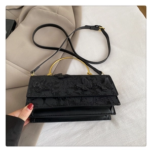 Détail du sac en dentelle noire avec appliques papillon 3D et poignée en anneau doré