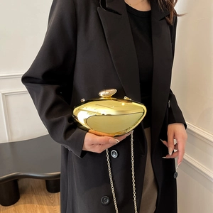 Modern gold metallic acrylic clutch bag with chain strap held by a person in a black blazer