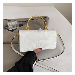 Détail du sac blanc à relief floral avec une élégante poignée ronde en métal doré