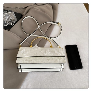 Détail du sac papillon en dentelle blanche avec poignée dorée et plis accordéon