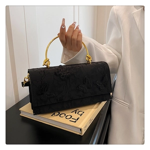 Détail d'un sac en dentelle noire avec broderie papillon 3D et poignée en anneau doré chic