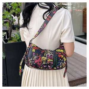 Detail of a black street style shoulder bag with colorful graffiti text worn by a model