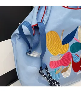 Close-up of adjustable strap and colorful fruit embroidery on a blue nylon tote bag