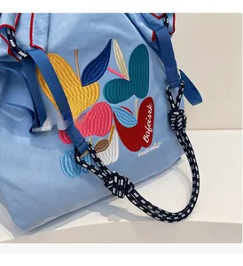 Detail of the braided shoulder strap and colorful apple embroidery on light blue tote