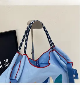 Detail of light blue embroidered tote bag with woven rope handles and red trim accents