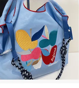 Detail of light blue tote bag featuring fruit embroidery and red contrast piping