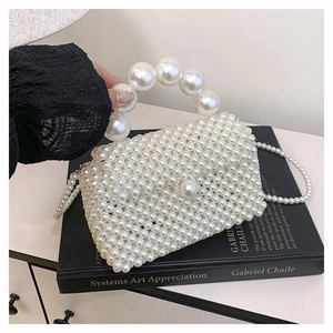 Détail du sac à main tressé en perles crème avec poignée de perles sur un livre