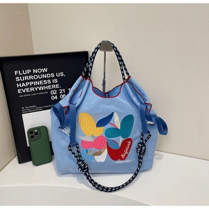 Detail of blue tote bag featuring fruit embroidery and braided rope handles