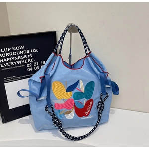 Detail of colorful leaf embroidery and woven handle on light blue nylon tote bag