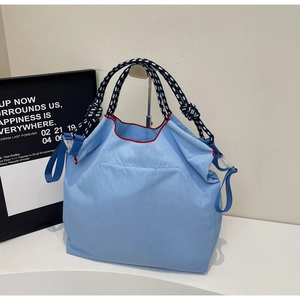 Macro detail of light blue nylon tote bag with woven rope handle and red trim accents