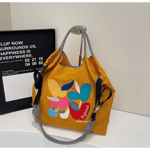 Detail of colorful apple embroidery on yellow canvas tote with checkerboard strap