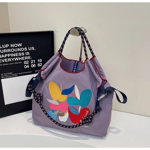 Detail of purple tote bag showing colorful fruit embroidery and contrast woven handles