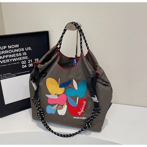 Detail of embroidered apple patterns on a gray canvas tote bag with woven rope handle