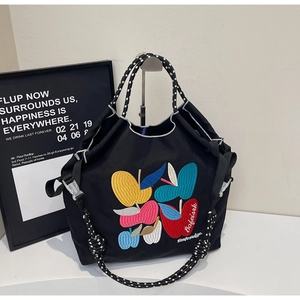 Detail of black tote bag with colorful apple embroidery and woven polka dot handle