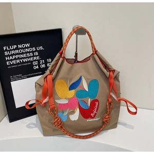 Detailed close-up of khaki tote bag with colorful apple embroidery and woven rope handles