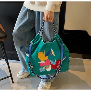 Close-up of green canvas tote bag with fruit embroidery and colorful drawstring straps