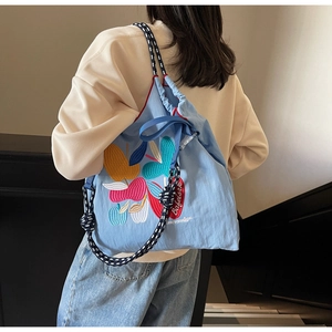 Detail of light blue canvas backpack featuring colorful apple embroidery and woven straps