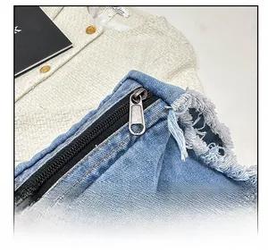Détail de la fermeture éclair en métal et des bords effilochés sur le sac en jean bleu