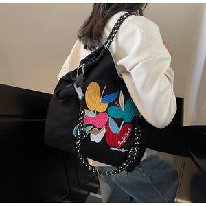 Detail of black drawstring canvas bag featuring colorful apple embroidery and woven straps