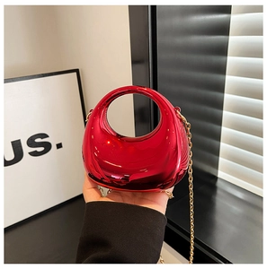 Detail of red acrylic crescent clutch bag featuring a sleek mirror finish and gold chain