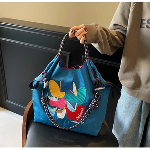 Detail of blue tote bag with colorful apple embroidery and tri-color woven handle