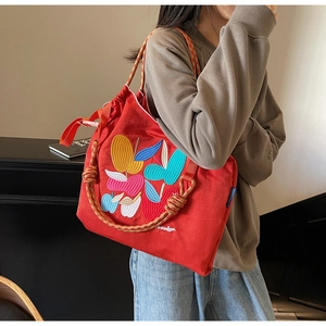 Detailed close-up of colorful apple embroidery on red canvas tote with braided rope handle