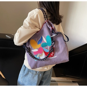 Detail of purple canvas drawstring backpack featuring colorful apple embroidery on bag