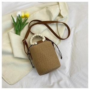 Detail of woven straw bucket bag showing wood bead handle and brown drawstring closure