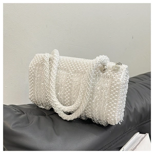 Detailed close-up of white pearl woven bucket bag with silver flower metal pendant