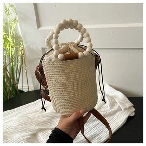 Detail of hand-woven straw bucket bag featuring large white wooden bead handle and drawstring