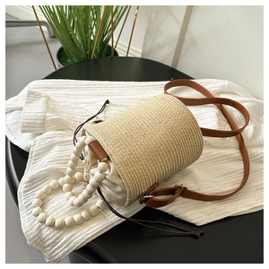 Detail of woven straw bucket bag with wooden beads handle and cream drawstring liner
