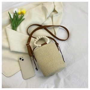 Detail of woven straw bucket bag featuring white beaded handle and brown drawstring closure