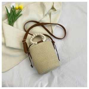 Detail of woven straw bucket bag featuring wooden bead handle and drawstring closure