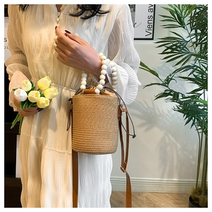 Detail of woven straw bucket bag featuring a white beaded handle and drawstring closure