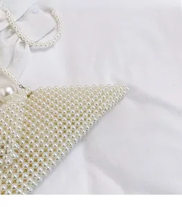 Close-up of a white pearl beaded triangle bag featuring large pearl strap accents