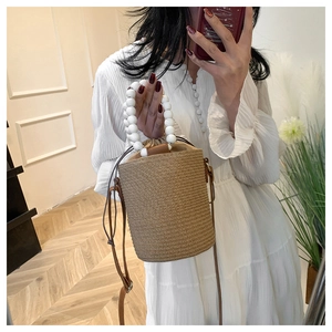 Detailed view of handwoven bucket bag with pearl beaded handle and brown leather strap