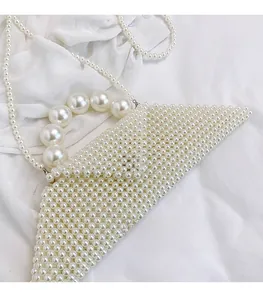 Detailed view of woven pearl handbag with top handle and strap on white fabric